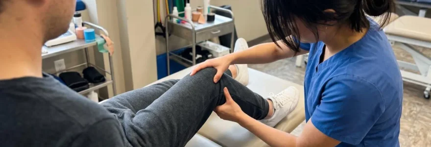A physiotherapist examining a patient's knee joint stability, hands positioned on the knee, patient seated on a treatment bench in a bright modern clinic
